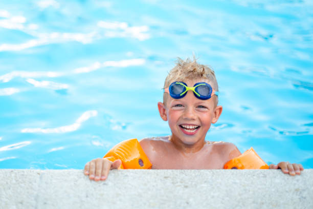 portrait garçon souriant en piscine, enfant en lunettes de bain et manches gonflables. vacances ou cours d’été à l’hôtel - summer sport equipment inflatable photos et images de collection