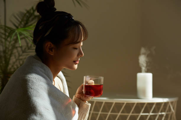 una giovane donna asiatica che si rilassa a casa bevendo tè alla frutta - aromaterapia foto e immagini stock