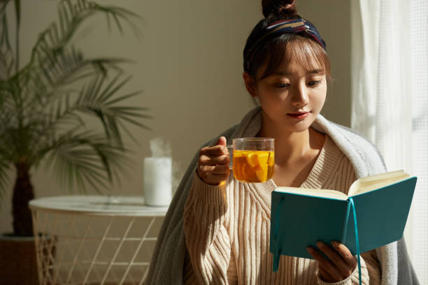 a young asian woman relaxing at home drinking fruit tea - afternoon tea fotos imagens e fotografias de stock