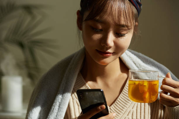 une jeune femme asiatique se relaxant à la maison en buvant du thé aux fruits - on the phone women beautiful beauty photos et images de collection