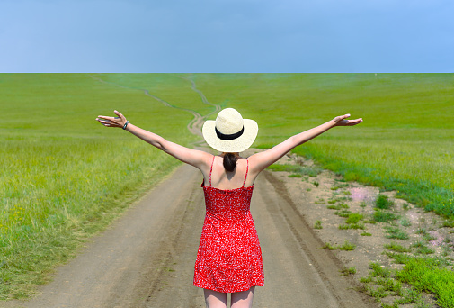 Young girl in red dress opened arms toward green field in summer