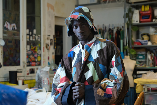 African man wearing traditional colorful clothes and hat at his sewing workshop.