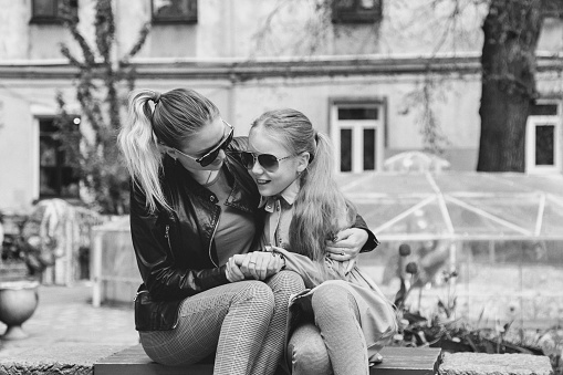 Happy pretty mother and little her cute daughter in casual clothes in bench near house in yard. Concept of spending time together with kids and family lovely relationships. Copy space for site