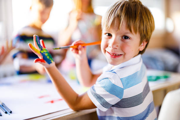 Smiling boy painting his hands whit watercolors at home