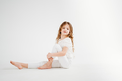 barefoot beautiful little girl with long hair in white clothes sits on the floor. children's photo shoot. cosmetics and shampoo for children's hair. children's clothing store