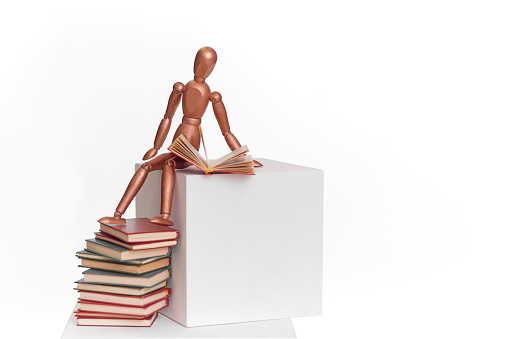 A wooden man sits on a stack of books.