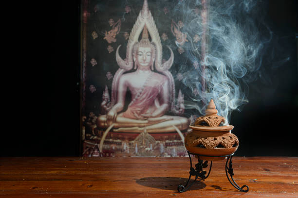 Incense cone burning with smoke on the dark background. Golden buddha zen meditation incense holder. Copy space.