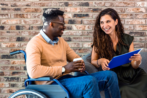 Man in a wheelchair communicates cheerfully with employees of the office during a business meeting