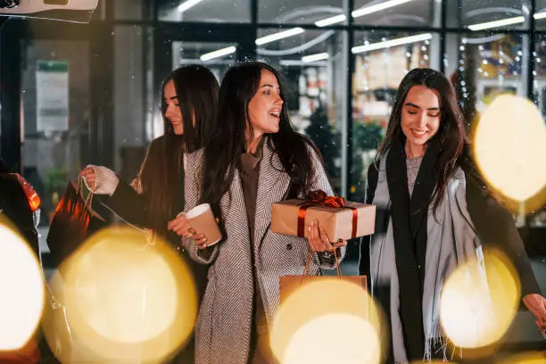 Photo of Cups of drink in hands. Three cheerful women spends Christmas holidays together outdoors. Conception of new year