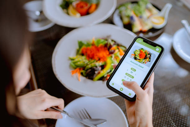 technology makes life so much easier for young asian woman using mobile app device on smartphone to place a food order in a restaurant. - food vegan food gourmet vegetarian food imagens e fotografias de stock