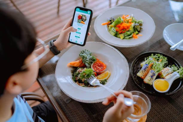 technology makes life so much easier for young asian woman using mobile app device on smartphone to place a food order in a restaurant. - food vegan food gourmet vegetarian food imagens e fotografias de stock