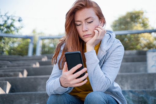 Worried young woman holding mobile phone waiting message