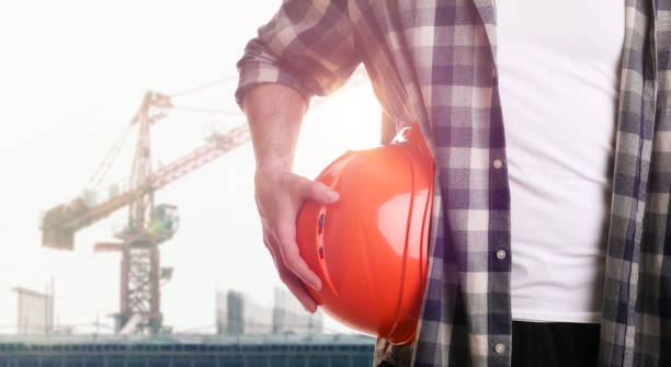 istock Man holding orange hard hat at construction site with unfinished building, closeup. Space for text 1331924610