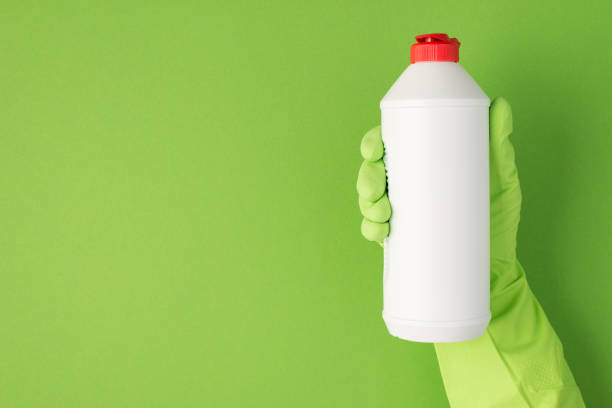 foto di mano in guanto di gomma verde che tiene una bottiglia di gel detergente bianco con cappuccio rosso senza etichetta su sfondo verde isolato con spazio di copia - chemical bottle cap chores foto e immagini stock