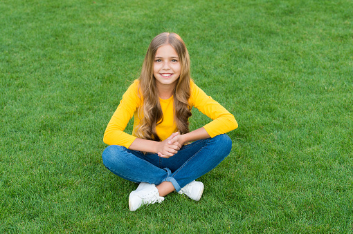 teen girl after hairdresser. relax on green grass. spring leisure time. happy childhood. kid with stylish hair. cheerful smile. happy little girl has long curly hair. kid beauty and fashion.