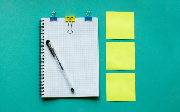 Three yellow stickers on a delicate blue background, a white notebook with a spiral and a pen to sirchu. Layout and flat lay with place for text. Concept back to school.
