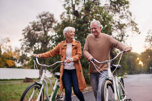 scatto di una coppia matura che si prende un giro in bicicletta al tramonto - mature adult bicycle senior adult heterosexual couple foto e immagini stock