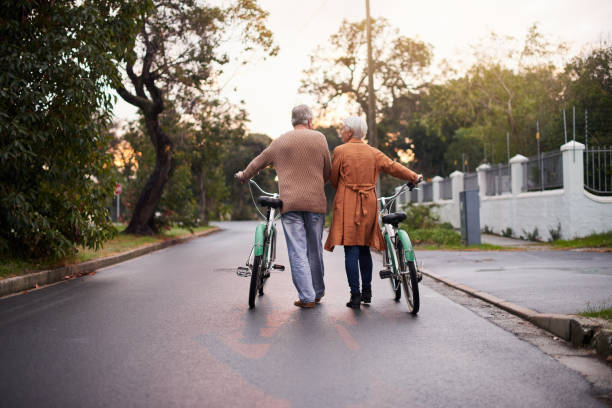 colpo di un maturo che cammina con le bici - mature adult bicycle senior adult heterosexual couple foto e immagini stock