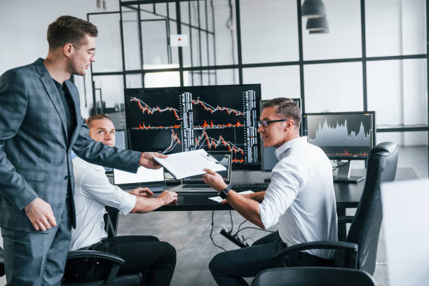 istock With documents. Team of stockbrokers works in modern office with many display screens 1331940742