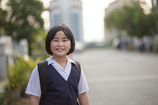 Asian Chinese girl with school uniform smiling looking at camera waiting school bas in front of house.
