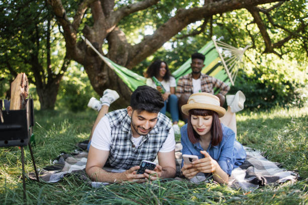 deux couples utilisant le mobile, discutant et buvant sur le pique-nique - hamac telephone homme photos et images de collection