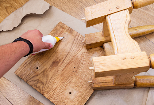 Home furniture repair. Hand applying glue to a broken oak stool.
