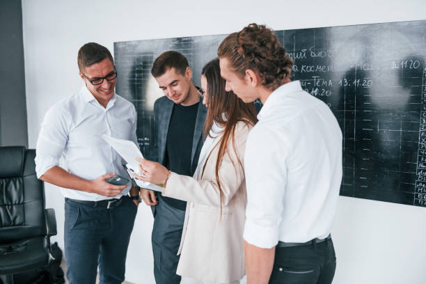 istock With documents in hands. Group of young smart people that standing near blackboard in office 1331948225