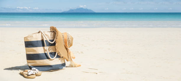 Stripy beach bag, straw hat and flip flops on tropical beach