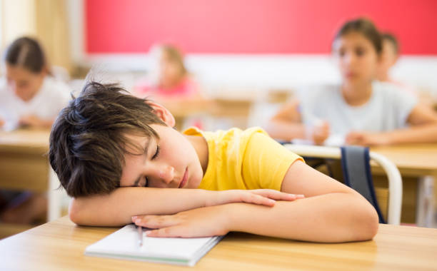 istock Bored tween boy sleeping at desk in classroom during lesson 1331952024