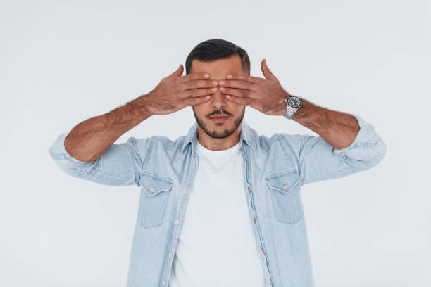 istock Covers his eyes. Young handsome man standing indoors against white background 1331952225
