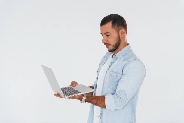 istock Uses laptop. Young handsome man standing indoors against white background 1331953267