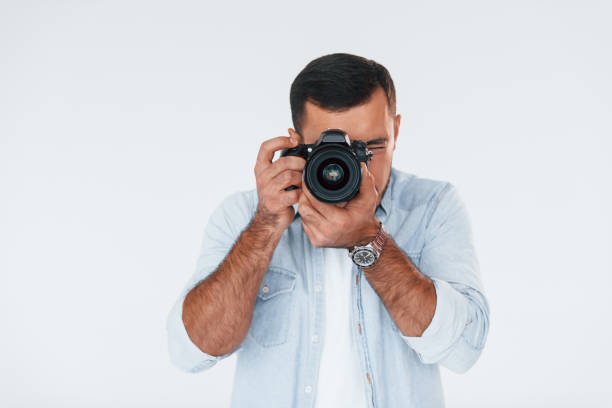 istock With professional camera. Young handsome man standing indoors against white background 1331953435