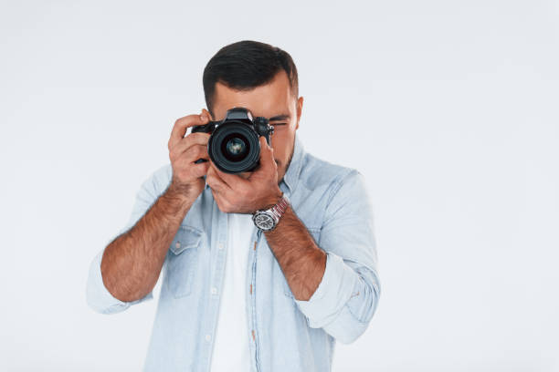 istock With professional camera. Young handsome man standing indoors against white background 1331953455