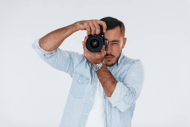 istock With professional camera. Young handsome man standing indoors against white background 1331953563