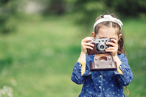 Little girl with old vintage camera making photos of surrounding nature in the park