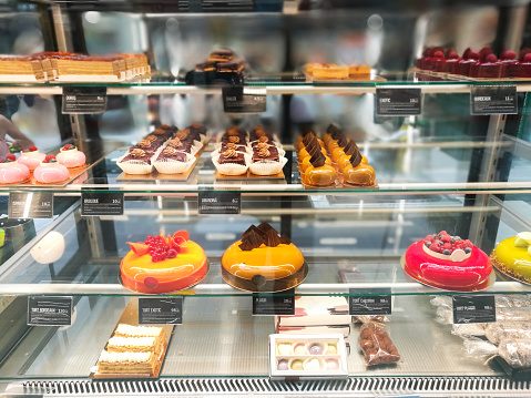 Color image depicting a variety of delicious cakes on display in the window of a bakery.