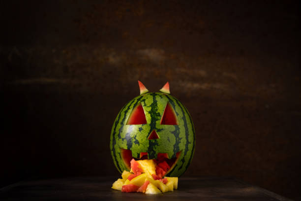 Funny watermelon eating pineapple. Watermelon throwing up. Tropical jack-o-lantern watermelon on dark background with pineapple pieces coming out of its mouth. Funny watermelon vomit. Space for text. pumpkin throwing up stock pictures, royalty-free photos & images