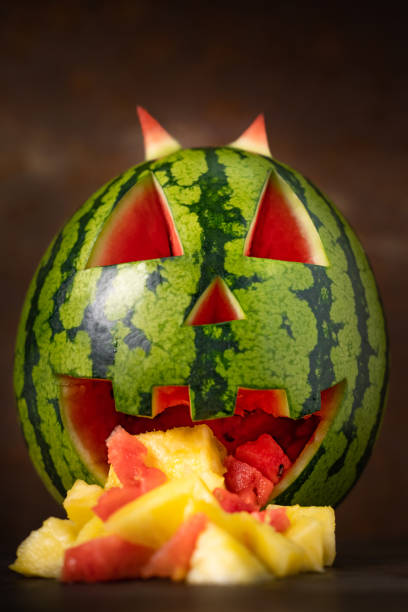 Funny watermelon eating pineapple. Watermelon throwing up. Tropical jack-o-lantern watermelon on dark background with pineapple bits coming out of its mouth. Funny watermelon vomit. Carved watermelon in a horror scene. throwing up pumpkin stock pictures, royalty-free photos & images