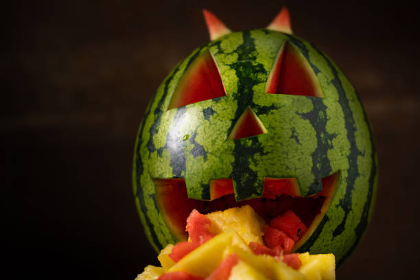 Funny watermelon eate pineapple. Watermelon throwing up. Tropical jack-o-lantern watermelon on dark background with pineapple pieces coming out of its mouth. Funny watermelon vomit. pumpkin throwing up stock pictures, royalty-free photos & images