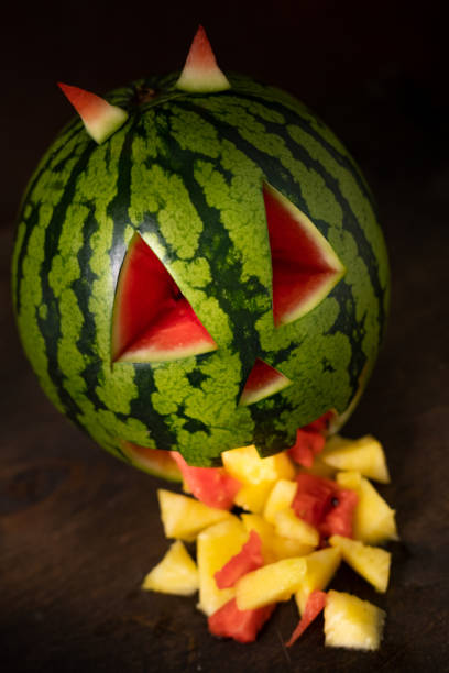 Funny watermelon eating pineapple. Watermelon throwing up. Tropical jack-o-lantern watermelon on dark background with pineapple bits coming out of its mouth. Funny watermelon vomit. pumpkin throwing up stock pictures, royalty-free photos & images