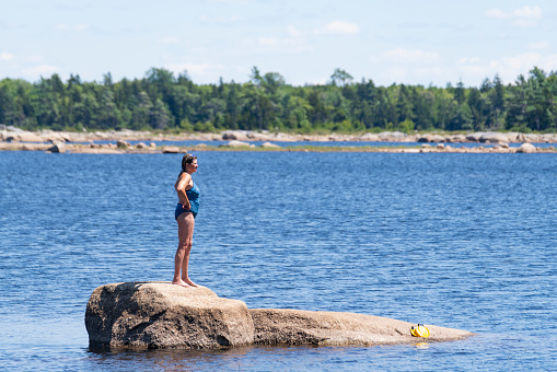 A mature woman standing on a rock in a lake.