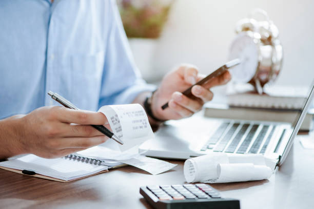 hombre joven sosteniendo la pluma con las cuentas que trabajan para calcular los datos del negocio, impuestos, pago de las cuentas, puesta en marcha contando las finanzas. concepto de contabilidad, estadística e investigación analítica - tasaciones fotografías e imágenes de stock
