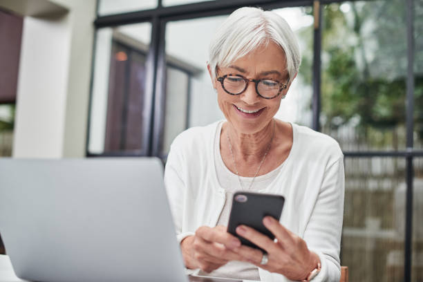 Shot of a senior woman using a laptop ad smartphone at home stock photo