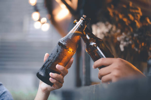 Cropped image of friends having fun clinking bottles of beer while resting at the pub stock photo