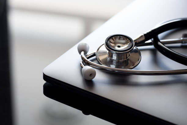 medizinisches stethoskop und laptop-computer auf dem schreibtisch - allgemeinarztpraxis stock-fotos und bilder