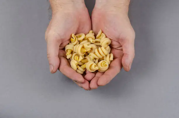 Nodi marini, insalatonde pasta. Dry uncooked pasta in male hands against a gray background. View from above at an angle.