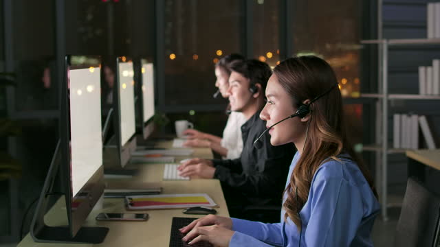 Hotline operator. Call center employees using a computer and headset at night in a modern office