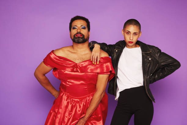 Androgynous male and female posing together Androgynous male and female posing together in studio. Gender queer man in female dress with woman in male clothing on purple background. androgyn stock pictures, royalty-free photos & images