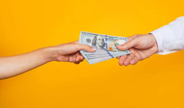 Young beautiful female hand gives a bunch of money to the male hand of a businessman for services stock photo
