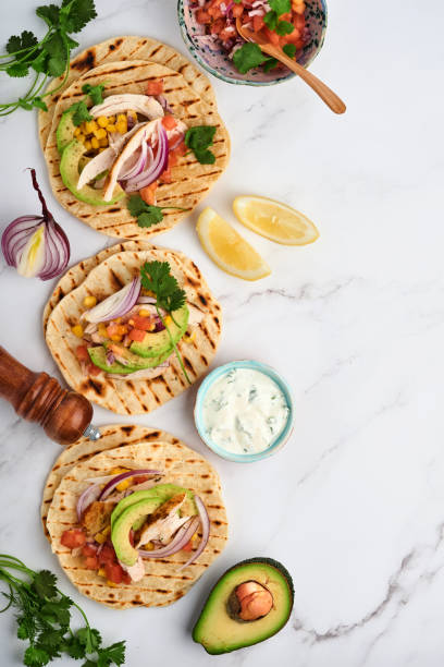 istock Mexican tacos with grilled chicken, avocado, corn kernels, tomato, onion, cilantro and salsa at white stone table. Traditional Mexican and Latin american street food. Top view. 1331972446